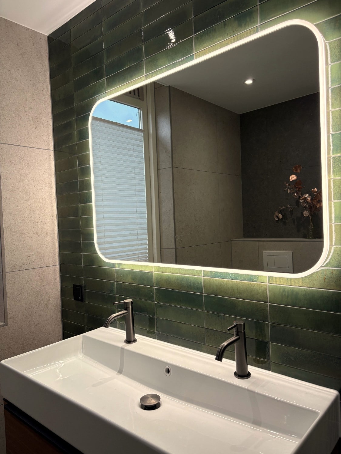 Miroir salle de bain aux coins arrondis sur un mur de carrelage vert